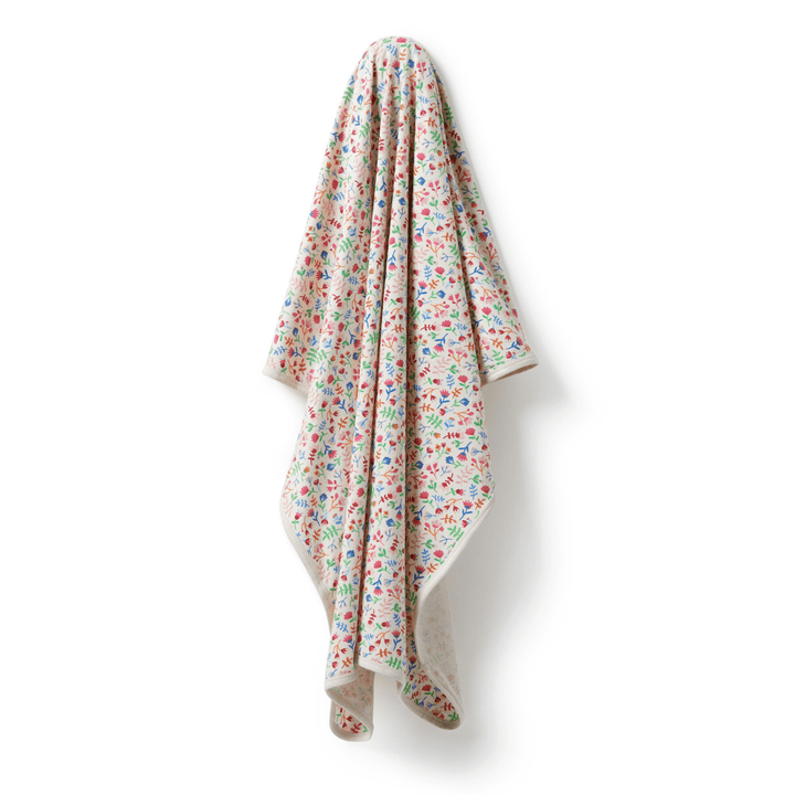 A Wilson & Frenchy Organic Baby Swaddle Blanket - LUCKY LAST - TROPICAL GARDEN ONLY hanging on a white wall.
