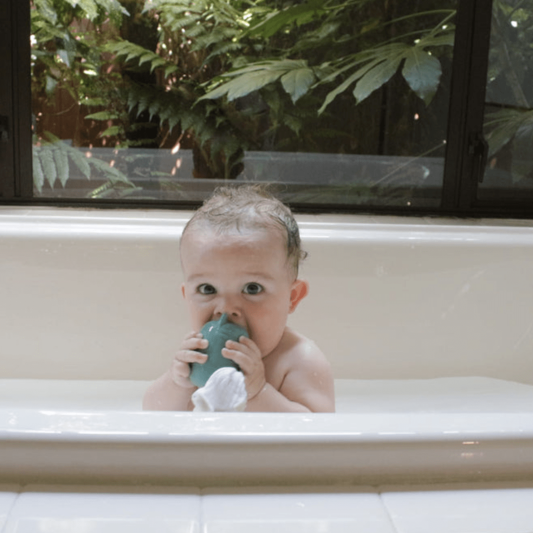 A baby is sitting in a bathtub with Classical Child Silicone Bath Toys Set (Multiple Variants), practicing fine motor skills while using a toothbrush.