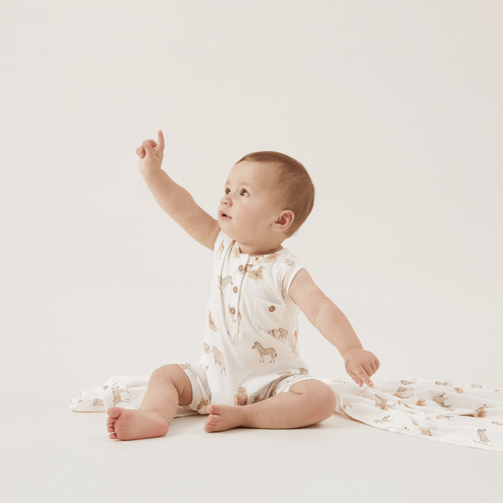 A baby is sitting on a white floor with an Aster & Oak Organic Cotton Zip Romper.