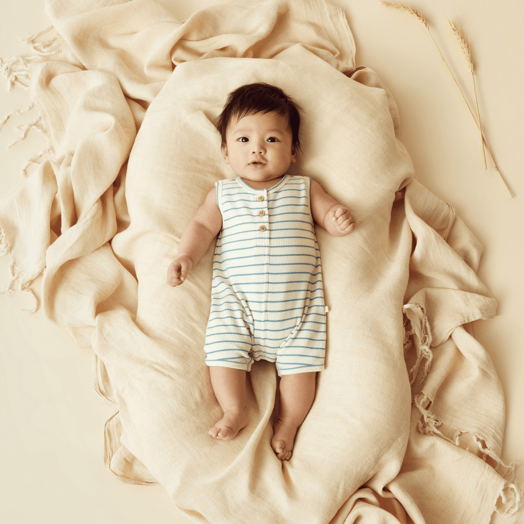 A baby in a Wilson & Frenchy Organic Rib Stripe Henley Growsuit in Lucky Last Petit Blue laying on an organic cotton blanket.