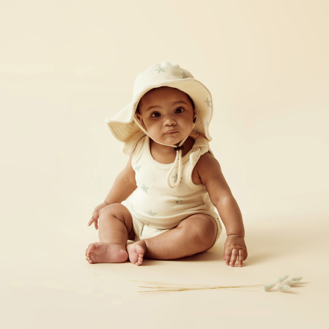 A Wilson & Frenchy Organic Terry Tie Singlet in a hat sitting on the ground, wearing an adorable Wilson & Frenchy Organic Terry Tie Singlet made from GOTS-certified organic fabric.