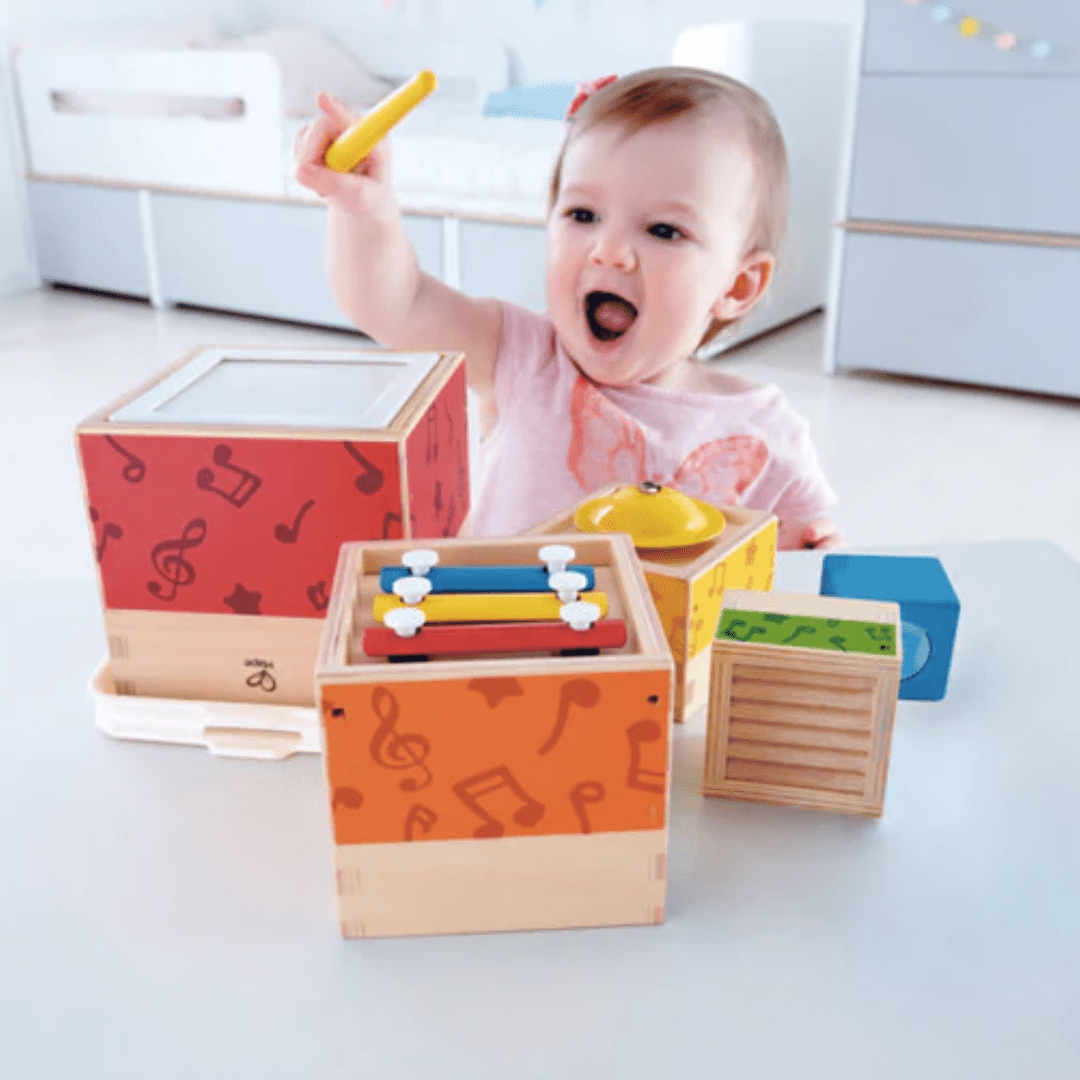 A baby is playing with a Hape Stacking Music Set by Hape, which includes musical stacking blocks and children's musical instruments.