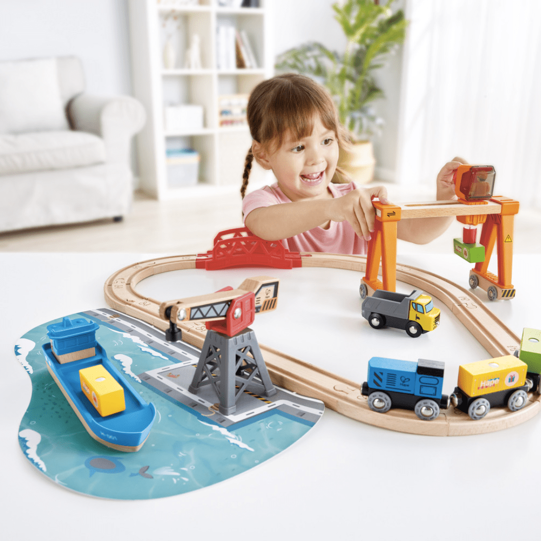 Happy-Girl-Playing-With-Hape-Life-And-Load-Harbour-Train-Set-Naked-Baby-Eco-Boutique