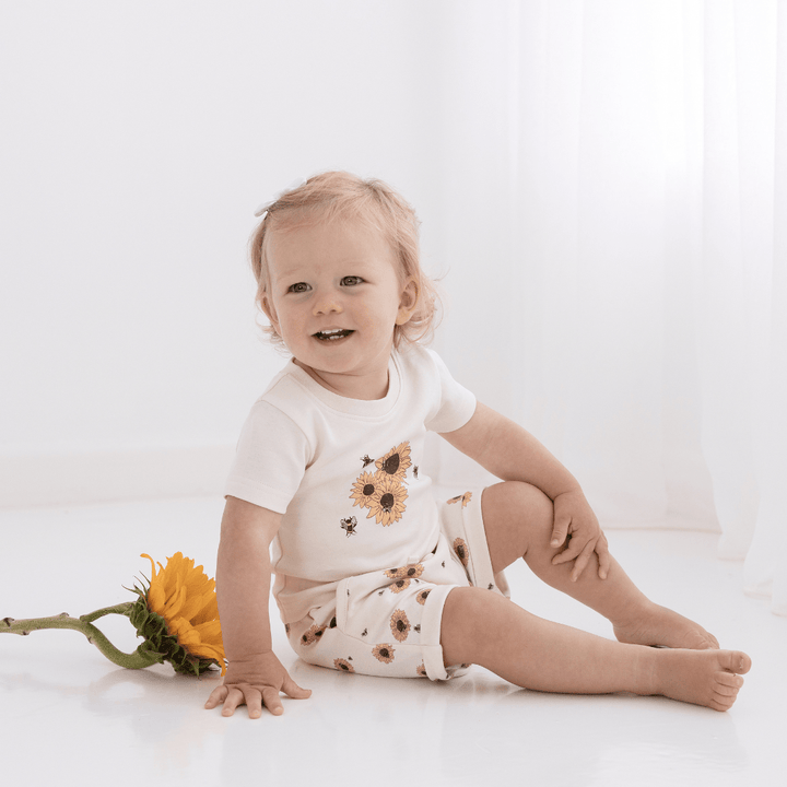 Happy-Girl-Sitting-With-Sunflower-Wearing-Aster-And-Oak-Organic-Cotton-Print-Top-Sunflower-Naked-Baby-Eco-Boutique