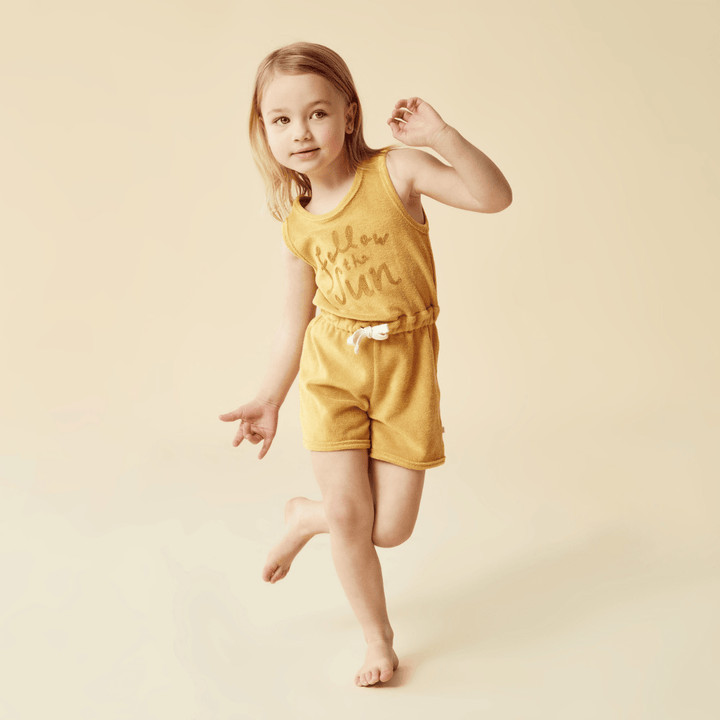 Wilson & Frenchy Organic Terry Kids Playsuit, a Wilson & Frenchy little girl in a yellow romper running on a beige background.