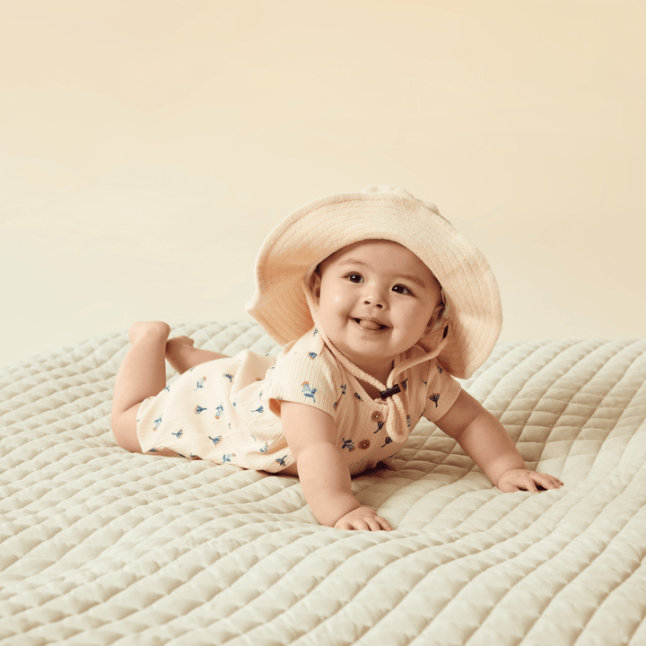 A baby lounging on a bed in a Wilson & Frenchy Organic Terry Sunhat - LUCKY LAST - SUN DIAL - 6-12 MONTHS.