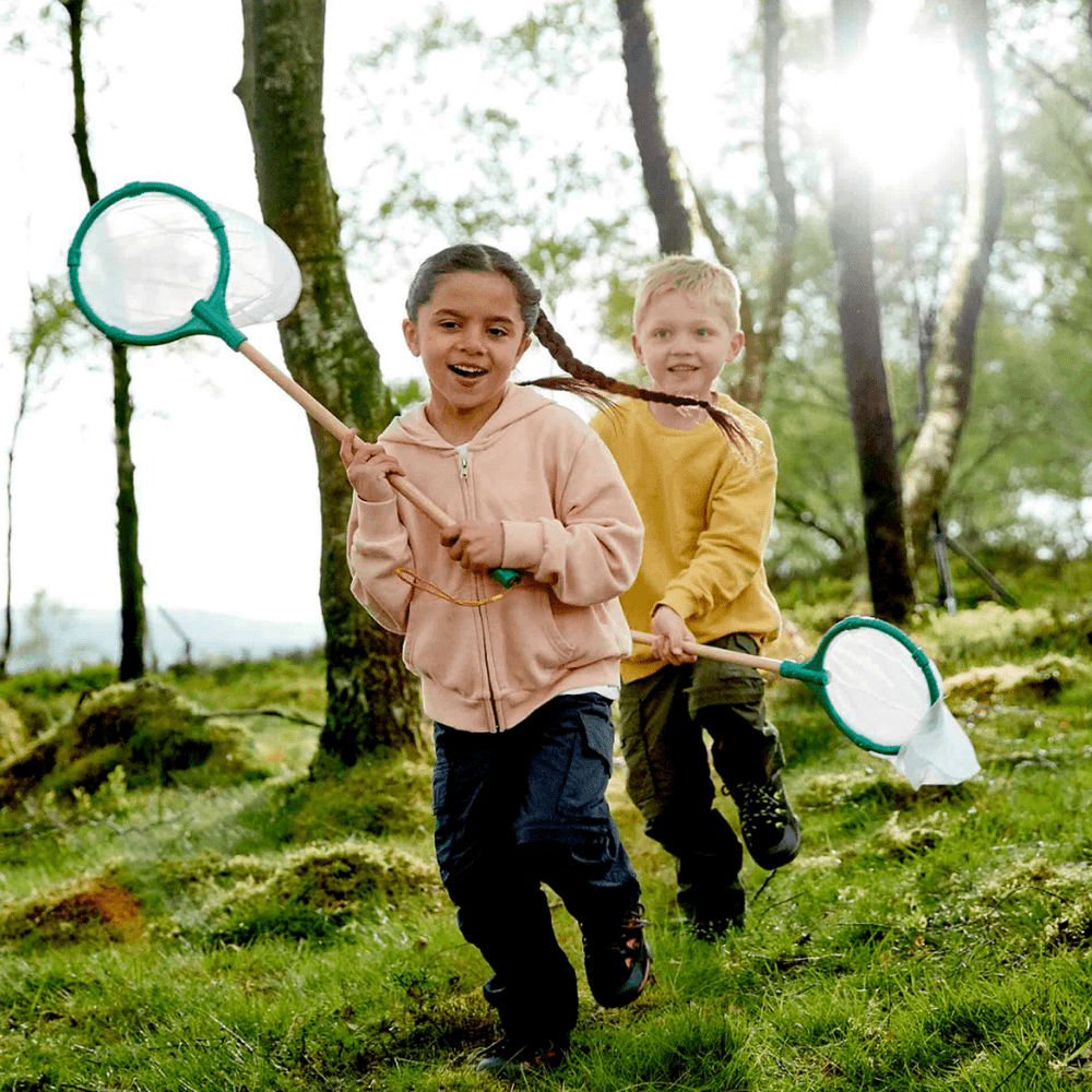 Two children with lightweight Hape butterfly nets running through the woods.