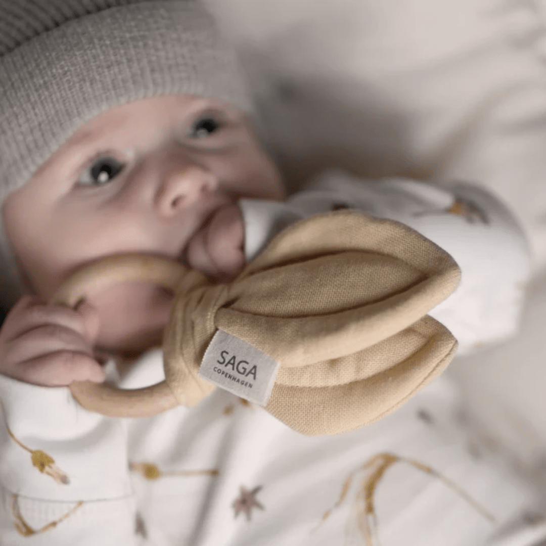 A baby wearing a beanie is chewing on a Saga Copenhagen Organic Cotton + Beechwood Teething Ring.