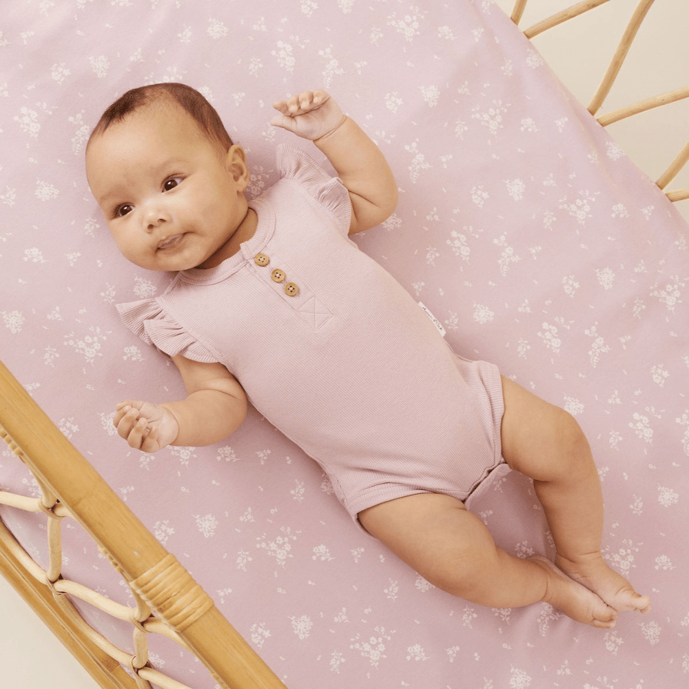 A baby lying in a crib with an Aster & Oak Organic Cotton Dawn Pink Rib Flutter Onesie.