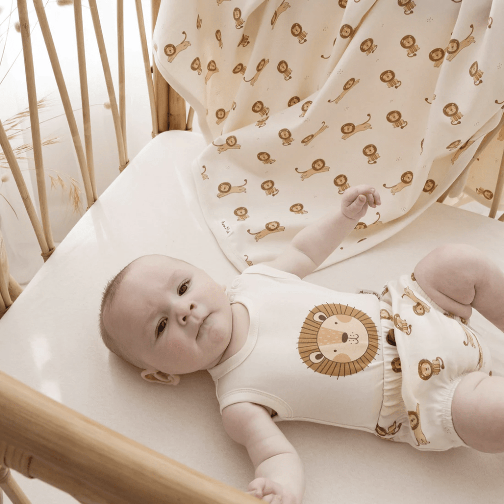 A baby laying in an Aster & Oak Organic Lion Print Singlet Onesie crib with a lion on it.
