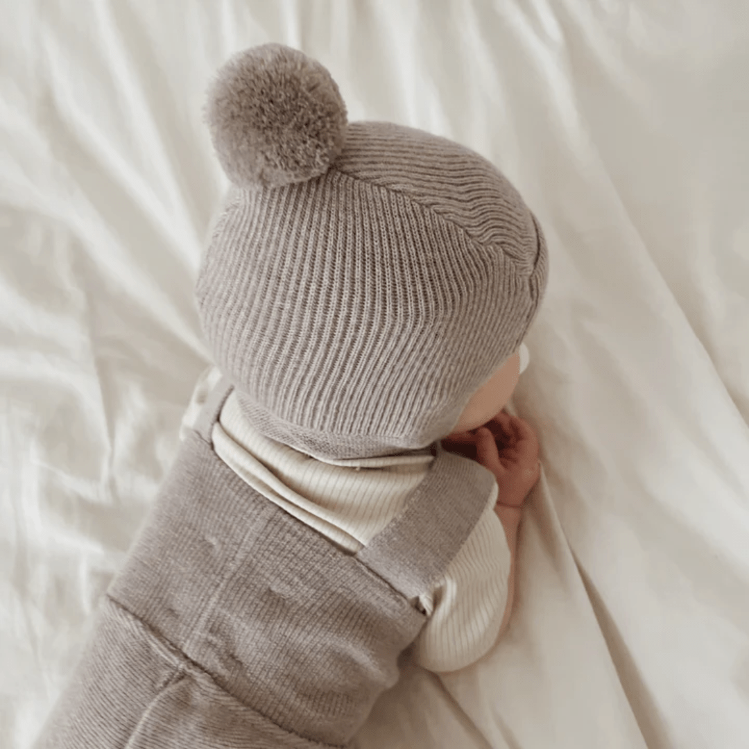 A baby is laying on a bed with a Saga Copenhagen Merino Bonnet.