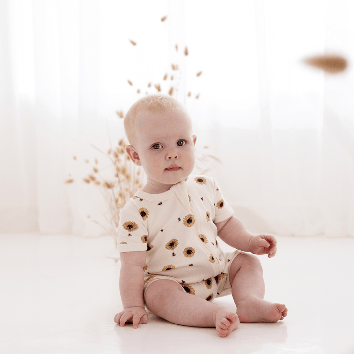 A baby sitting on the floor in a white Aster & Oak Organic Cotton Zip Romper.