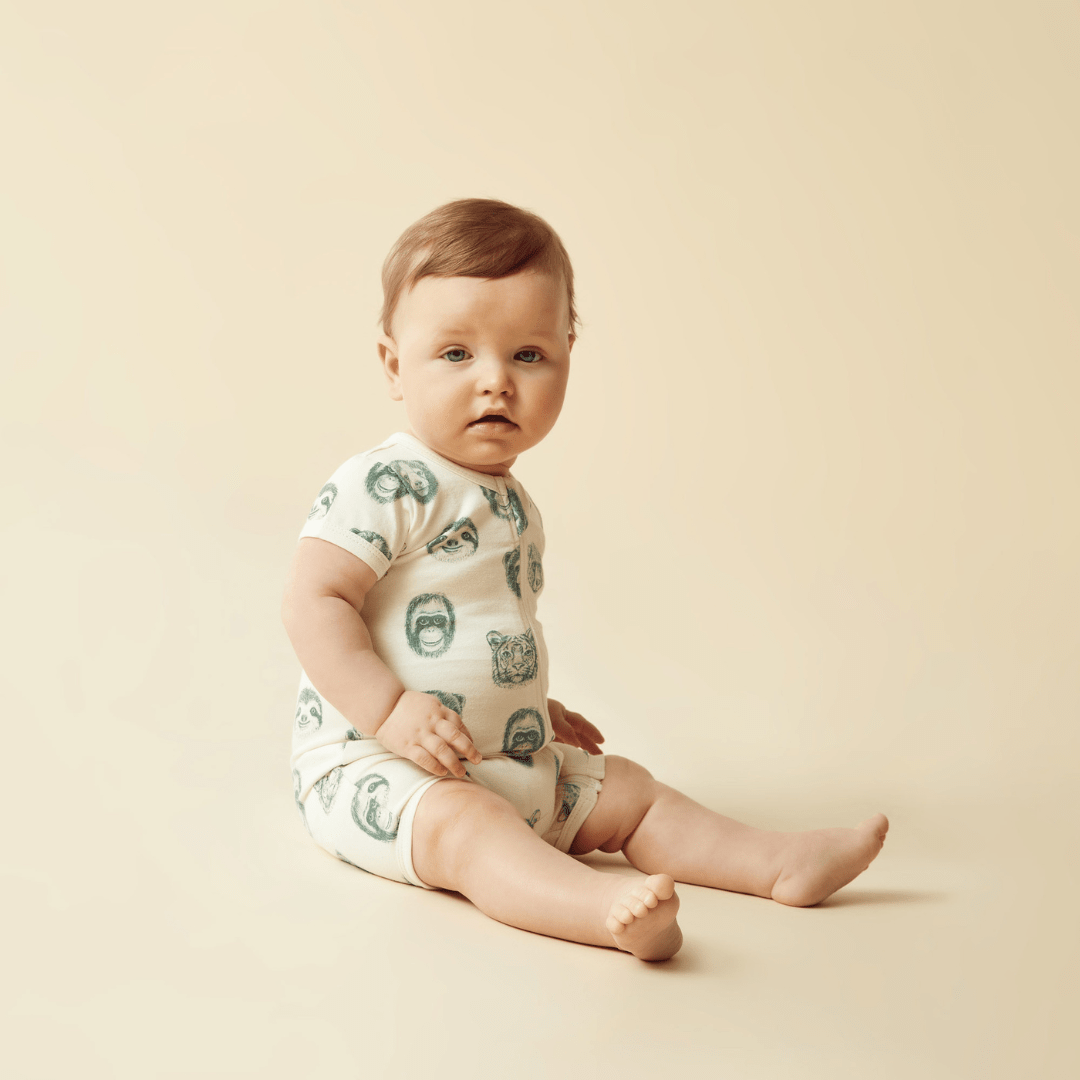A baby sitting on the floor in a green Wilson & Frenchy Organic Boyleg Zipsuit.
