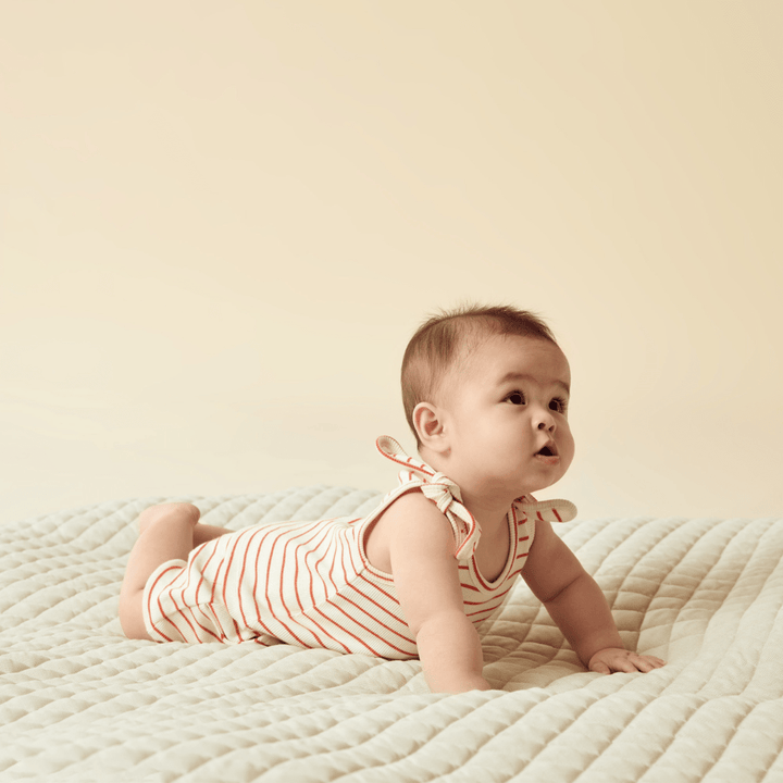 A baby laying on a bed in a Wilson & Frenchy Organic Rib Stripe Tie Singlet (Multiple Variants) made of GOTS-certified organic cotton.
