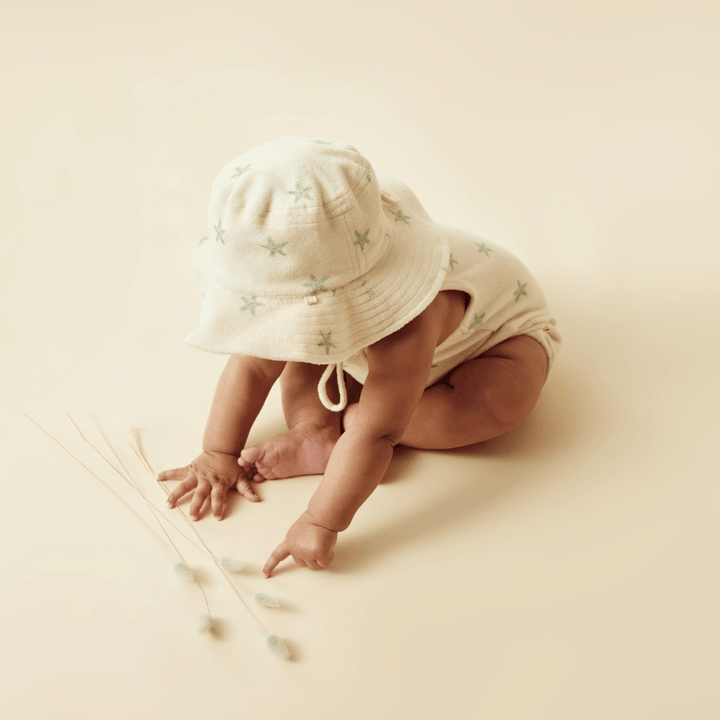 A baby wearing a Wilson & Frenchy Organic Terry Sunhat - LUCKY LAST - SUN DIAL - 6-12 MONTHS and sticks.