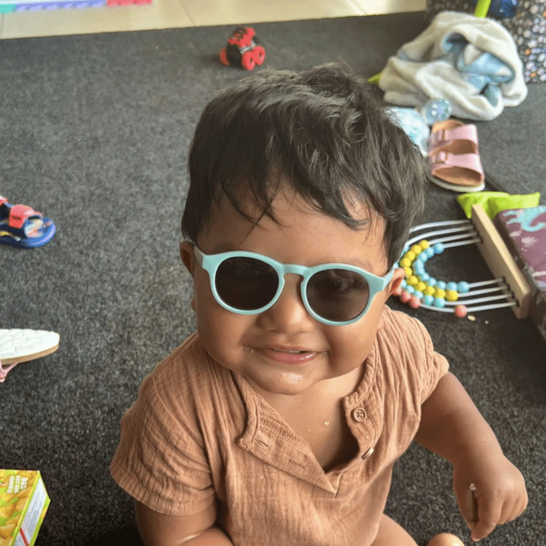 A baby wearing Zazi Shades Baby & Toddler Sunglasses in a room full of toys, enjoying the polarized clarity and UV400 protection.