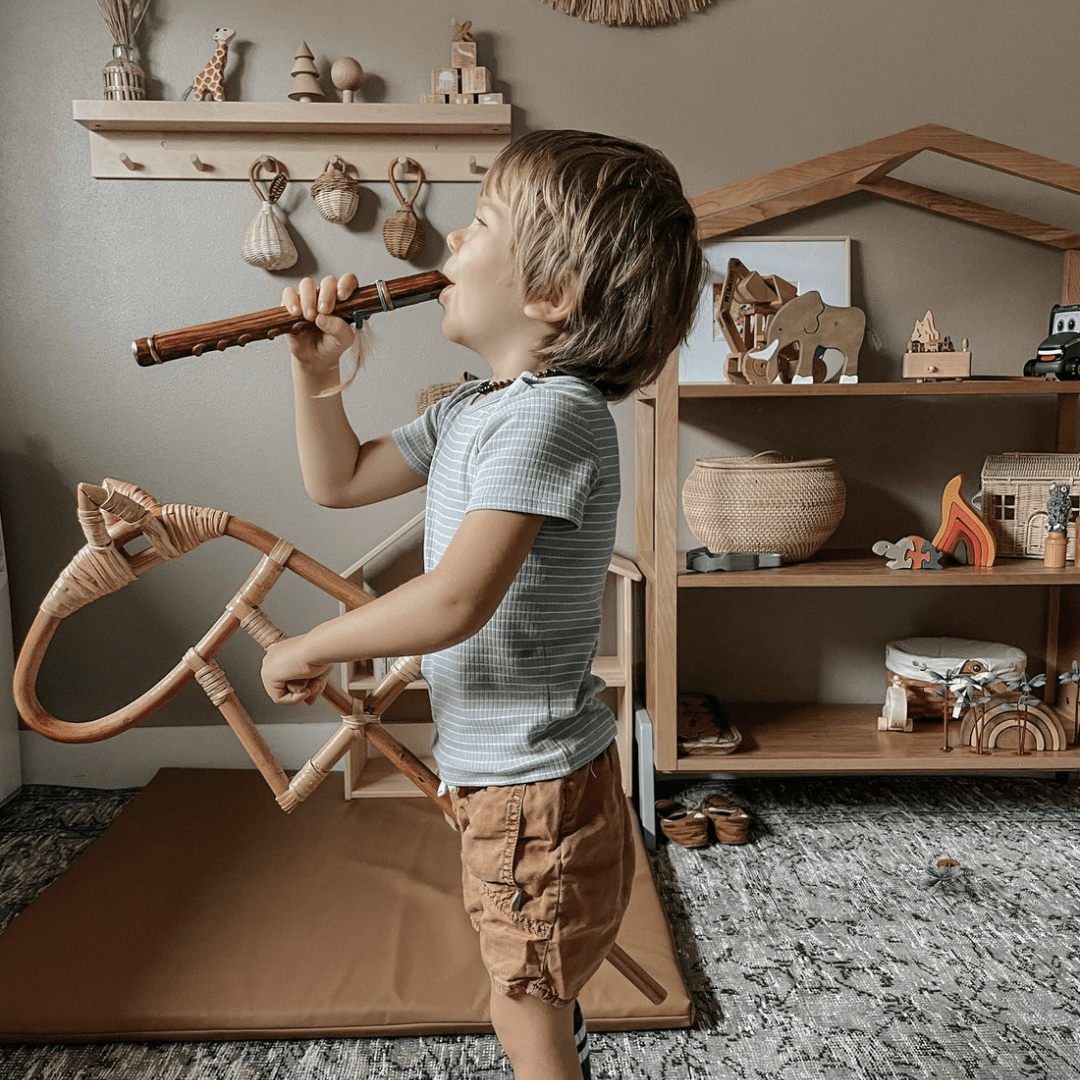 A young boy having imaginative fun playing with a Classical Child wooden flute in a toy room.