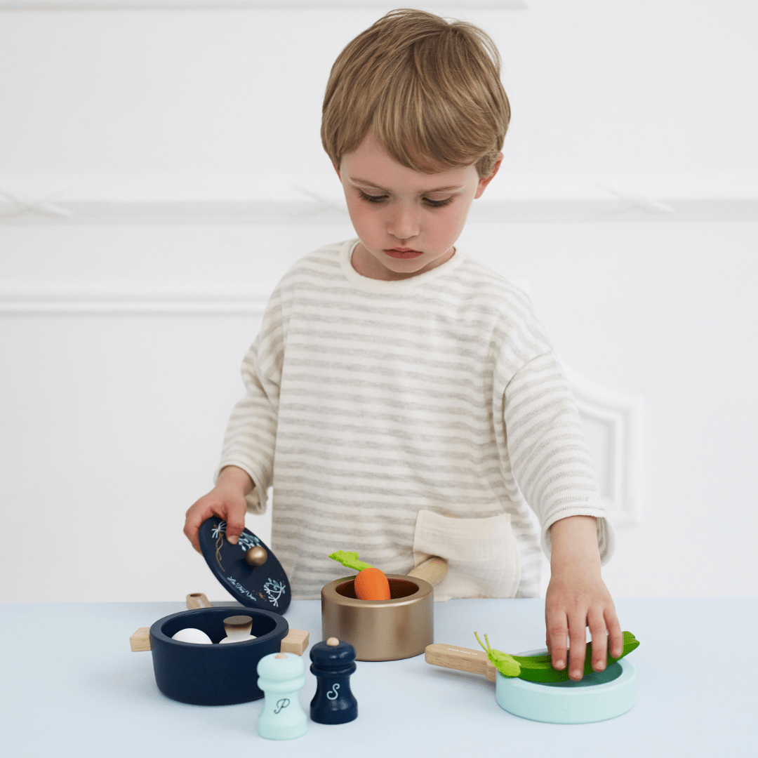 A young boy is playing with a Le Toy Van Pots & Pans cooking utensils set made from sustainable rubberwood.
