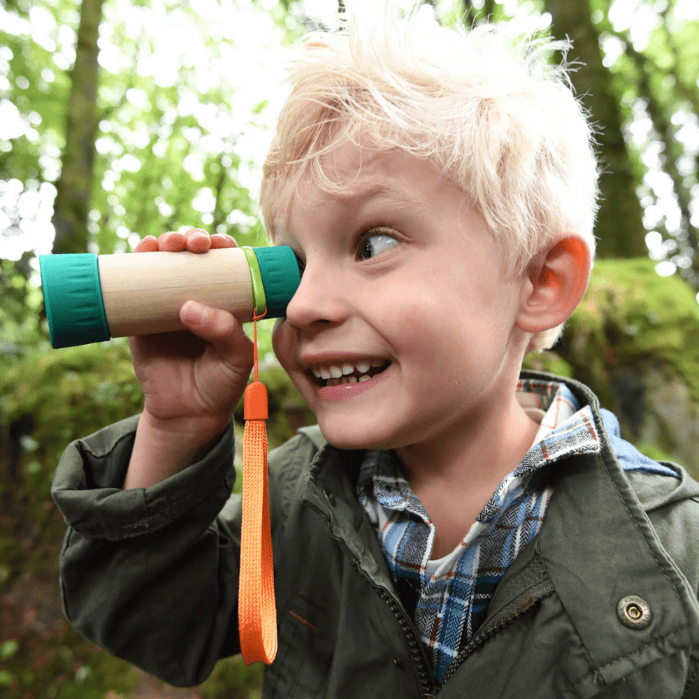 A young boy, equipped with an eco-friendly and adjustable Hape Adjustable Telescope, explores the enchanting woods through his binoculars.