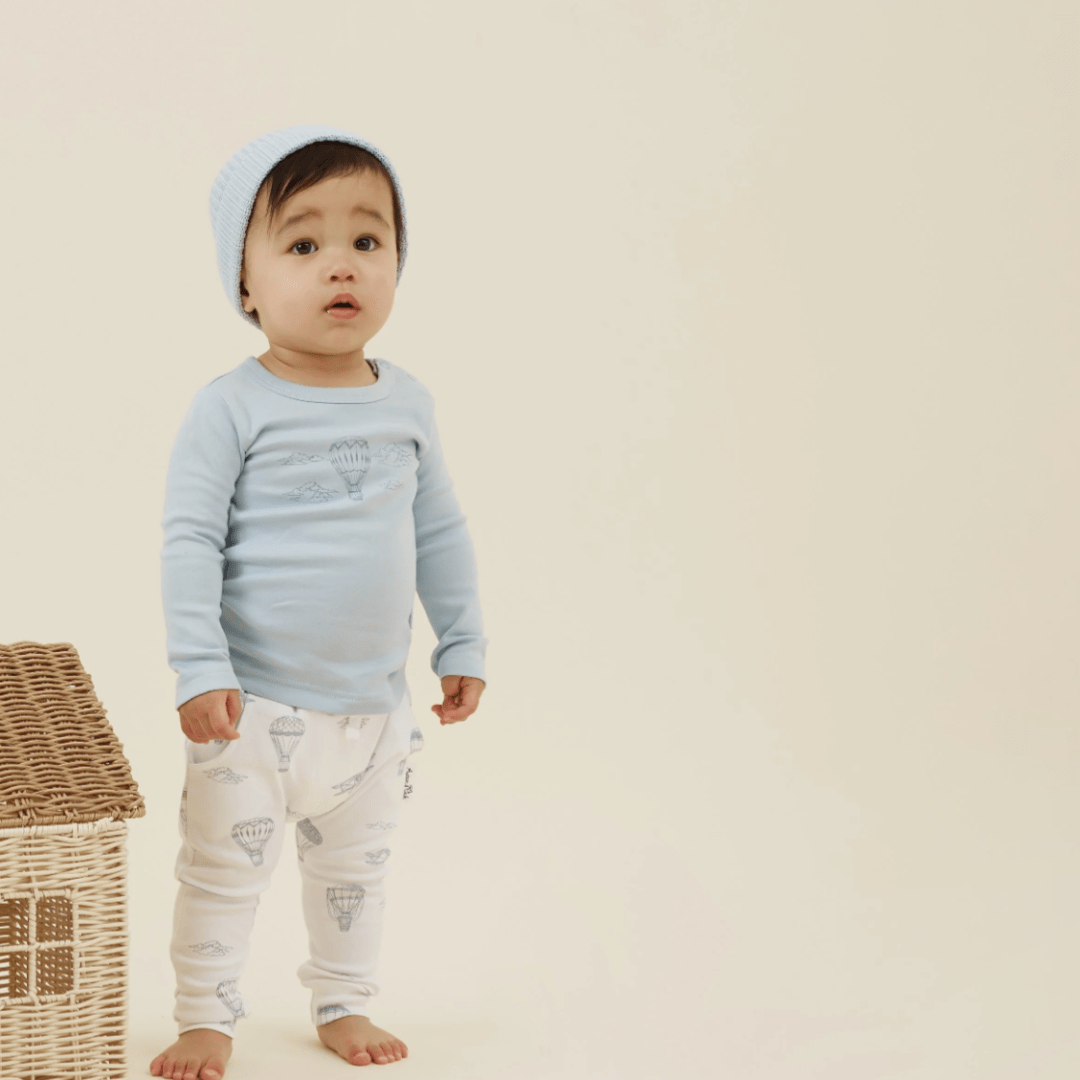 Toddler in a blue outfit and an Aster & Oak Organic Knit Beanie standing next to a wicker basket.