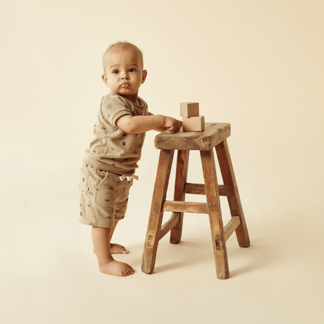 An adorable baby donning a Wilson & Frenchy Organic Terry Sweat Top while confidently standing on a wooden stool.