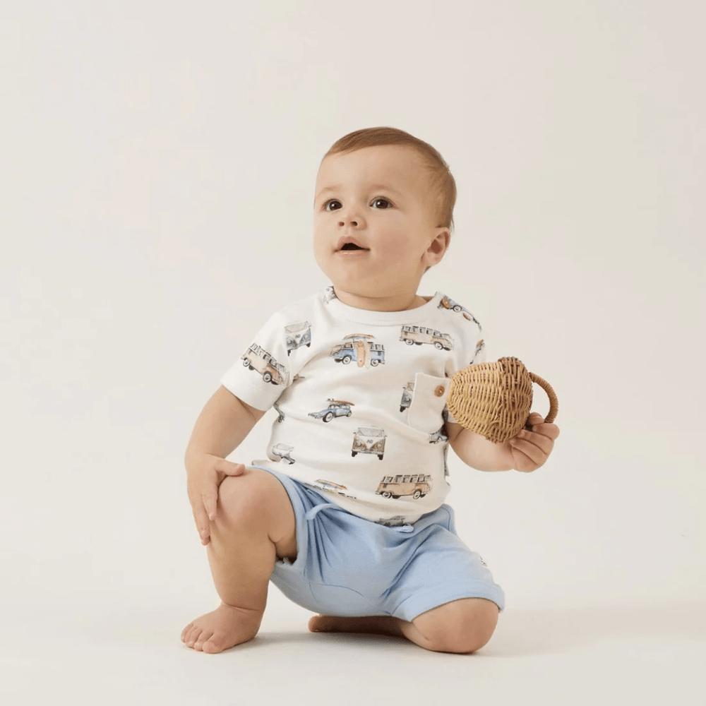 A baby is sitting on the floor holding a wooden bowl wearing Aster & Oak Organic Chambray Harem Shorts with an adjustable drawstring.