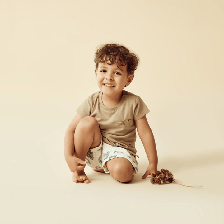 Young child crouching and smiling with a toy mouse on a beige background, wearing Wilson & Frenchy Organic Cotton Kids Shorts - LUCKY LASTS - HELLO JUNGLE - 5 YEARS ONLY.