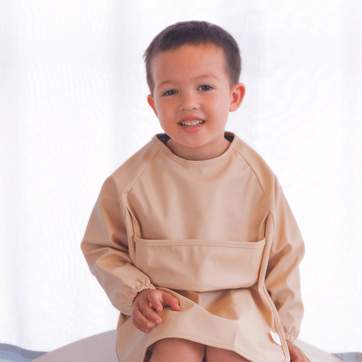 A young boy wearing a Zazi Recycled Full-Sleeved Bib (Multiple Variants) apron.