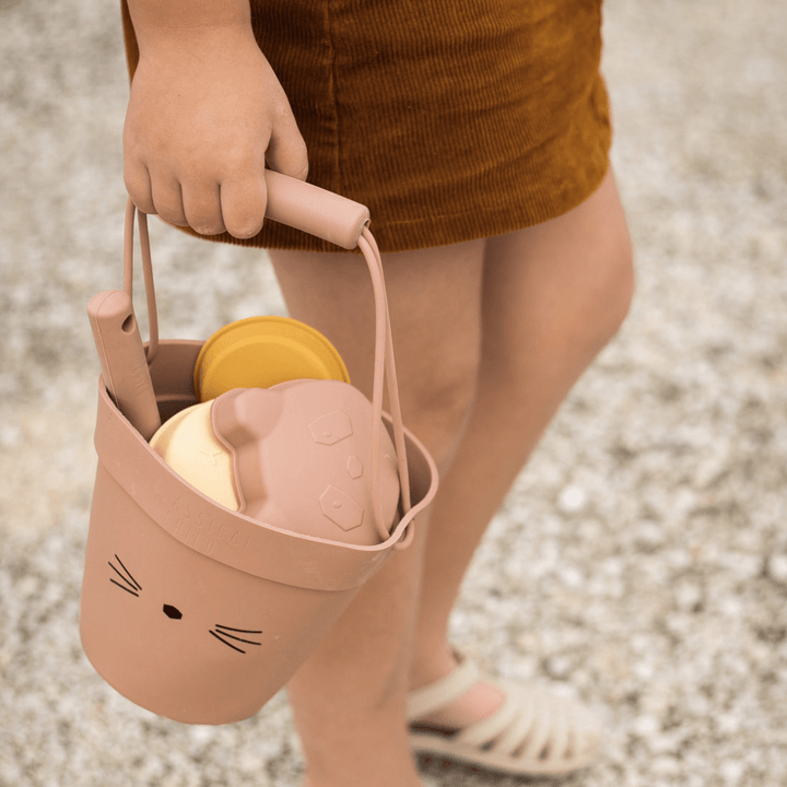 A girl holding a Classical Child silicone sand set with a cat on it, suitable for beach play.