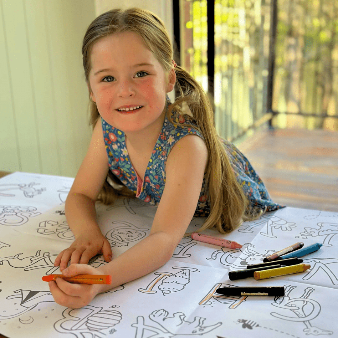 A little girl expressing her creativity at a table using Honeysticks pure beeswax crayons and the Honeysticks Jumbo Poster & Crayon Activity Set.