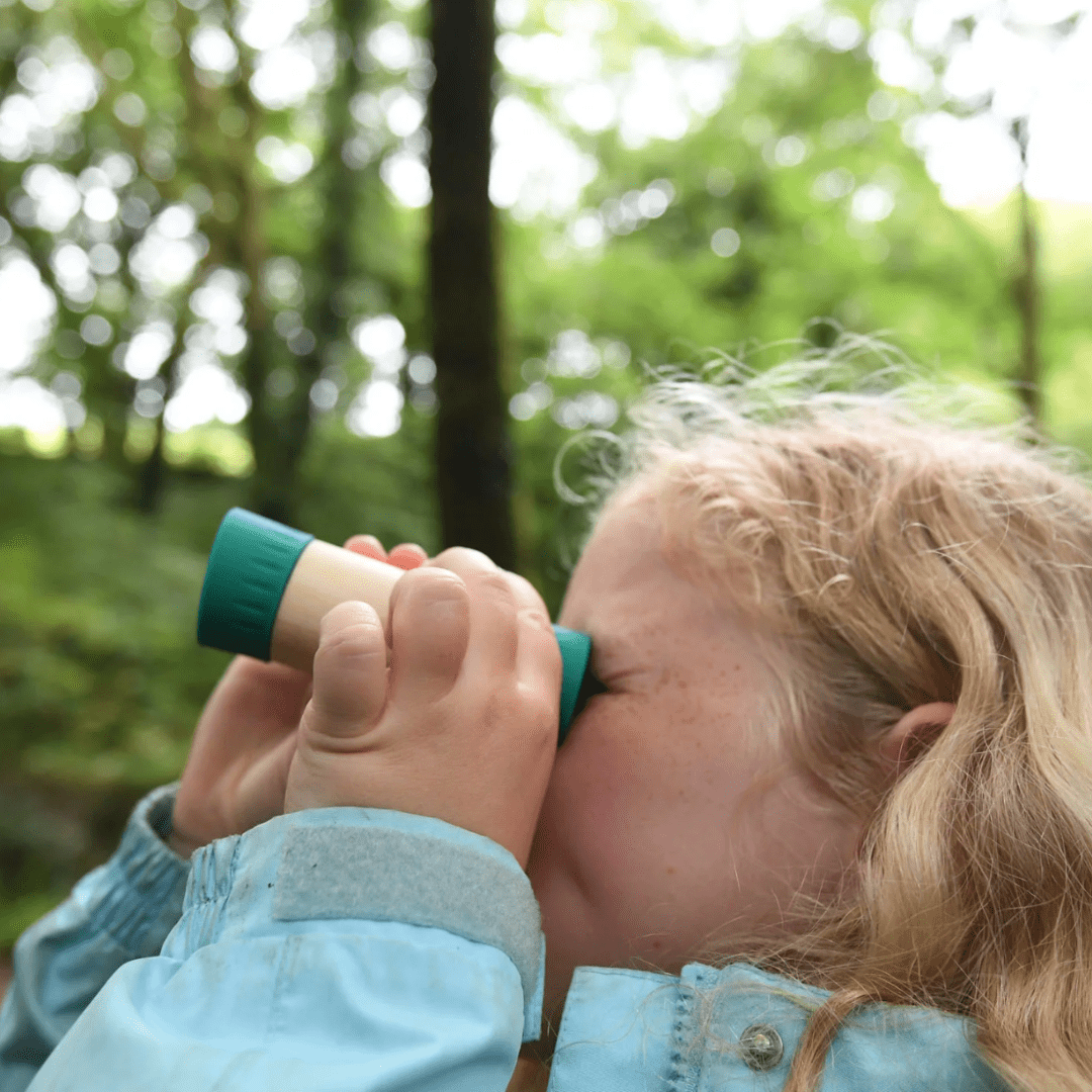 A little girl using the Hape Adjustable Telescope to explore the eco-friendly woods.