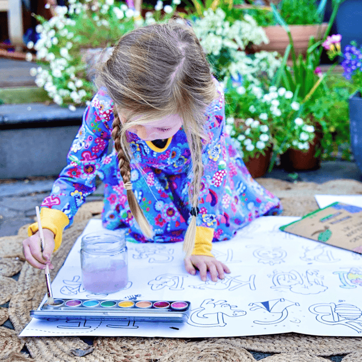 A little girl is using Honeysticks Jumbo Poster & Watercolour Paints Activity Set, a product by Honeysticks, to draw on a piece of paper.