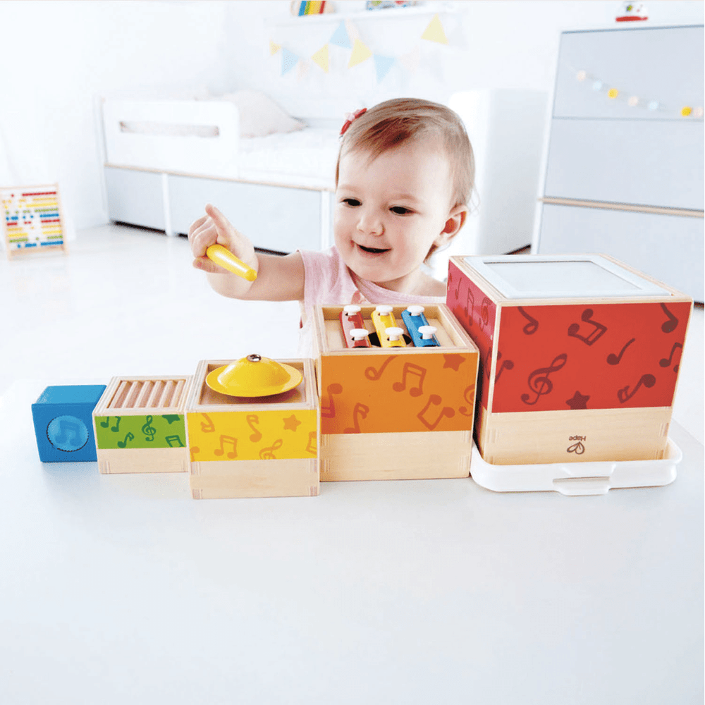 A baby is playing with the Hape Stacking Music Set in a room.