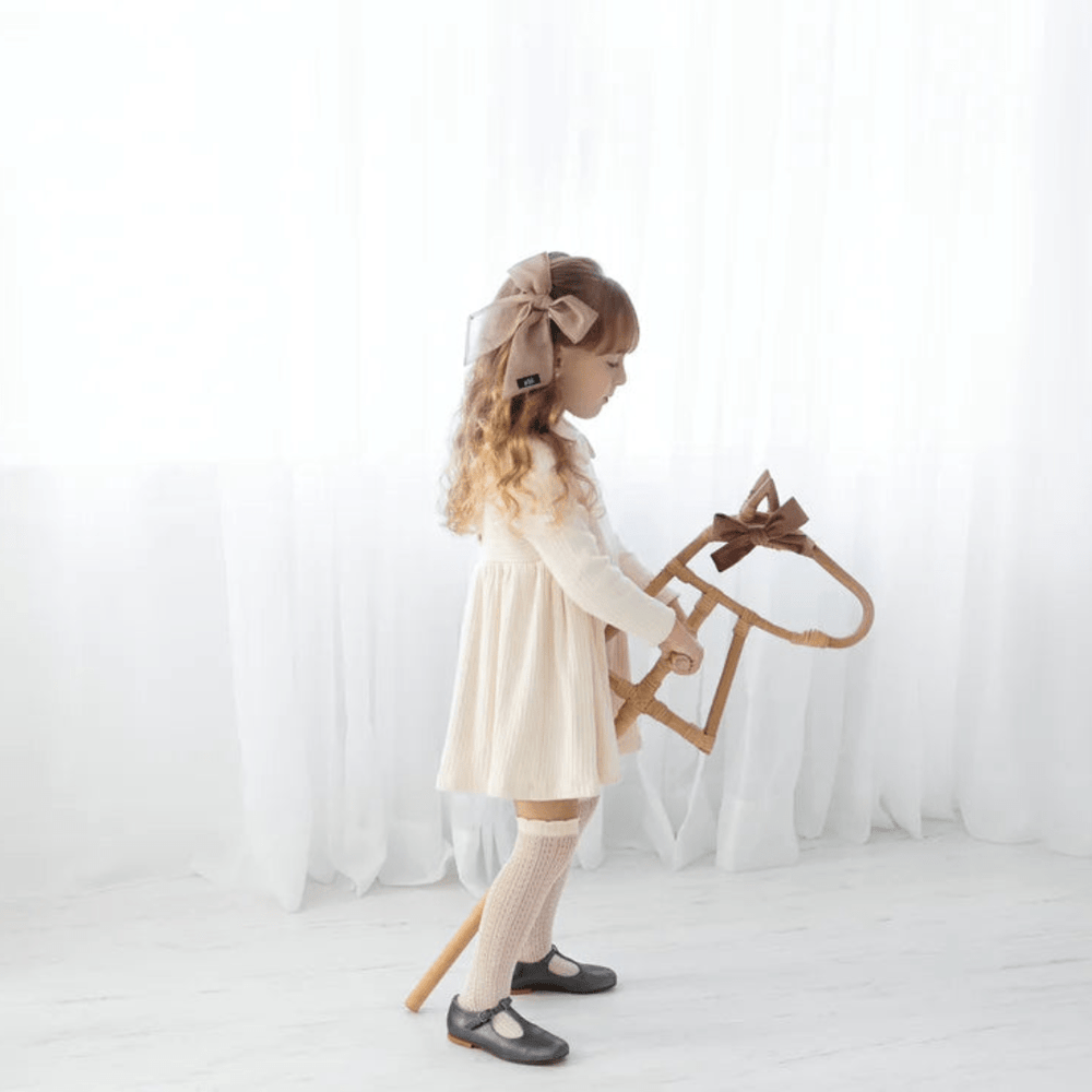 An eco-responsible little girl in a dress engaging in imaginative fun with her Classical Child Rattan Hobby Horse.