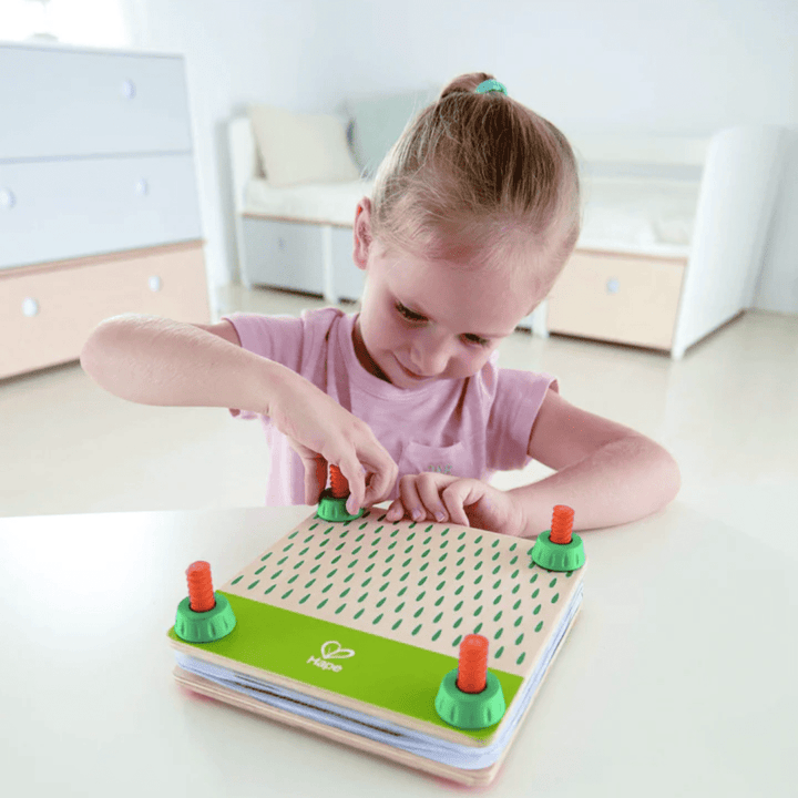 A little girl playing with a Hape Flower Press Art DIY Kit wooden toy on a table.