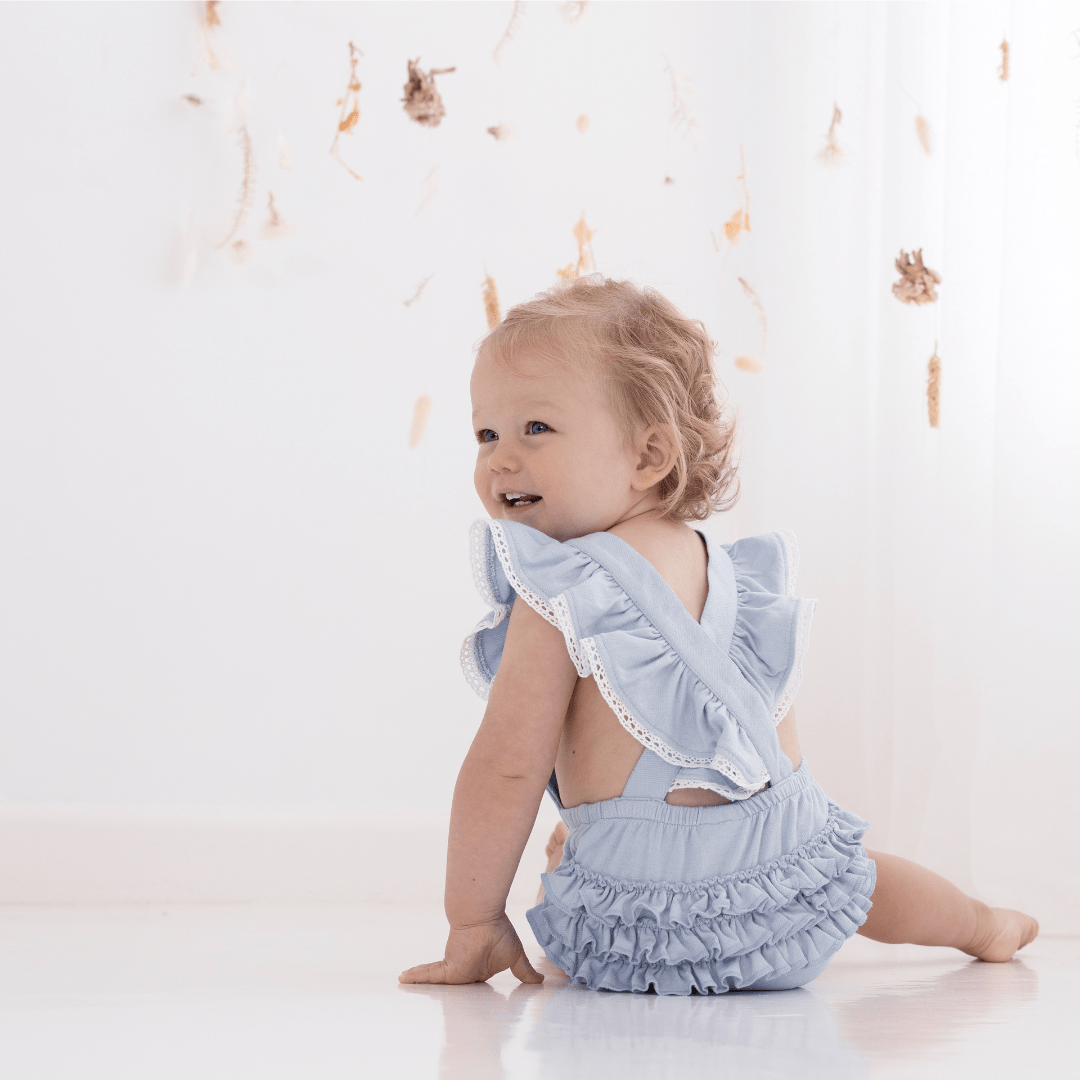 Little-Girl-Showing-Back-Of-Aster-And-Oak-Organic-Cotton-Chambray-Ruffle-Playsuit-Naked-Baby-Eco-Boutique
