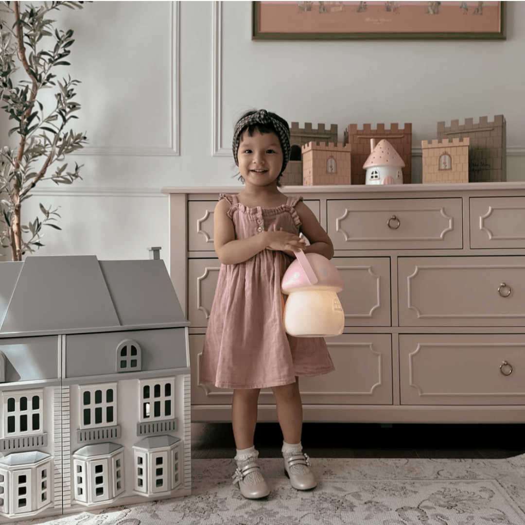 A little girl in a pink dress standing next to a Little Belle Nightlights Fairy House Carry Lantern by Little Belle Nightlights.