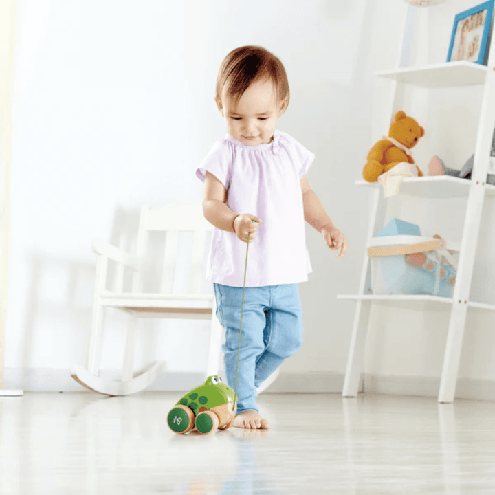 Little-Girl-Taking-Frog-For-A-Walk-With-Hape-Pull-Along-Toy-Frog-Naked-Baby-Eco-Boutique
