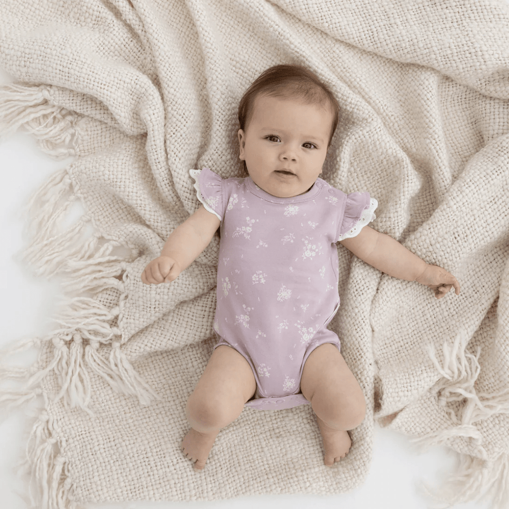 A baby is laying on a blanket with a purple Aster & Oak Organic Cotton Willow Floral Flutter Onesie.