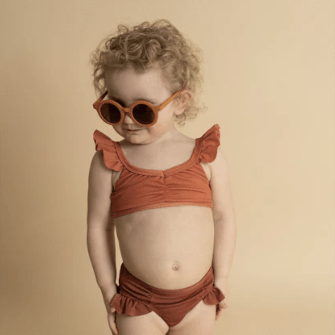 Little-Girl-Wearing-Glasses-And-Grech-And-Co-2-Piece-UPF-50-Recycled-Swimsuit-Melon-Sienna-Naked-Baby-Eco-Boutique