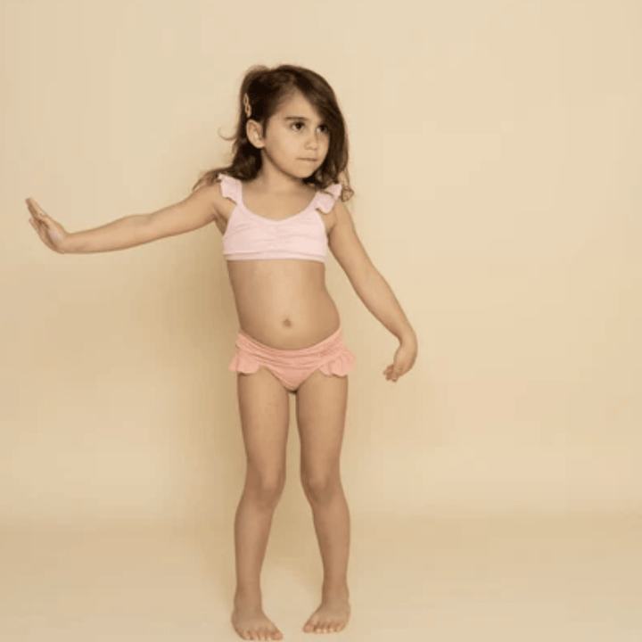 Little-Girl-Wearing-Grech-And-Co-2-Piece-UPF-50-Recycled-Swimsuit-Blush-Bloom-Coral-Rouge-Naked-Baby-Eco-Boutique