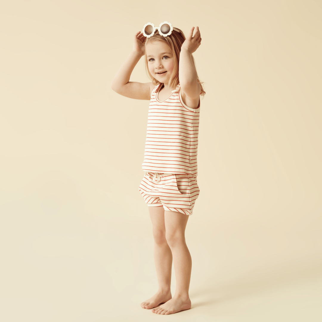 Wilson & Frenchy presents a little girl wearing a striped top and shorts, complemented by the Wilson & Frenchy Organic Rib Stripe Tie Kids Singlet (Multiple Variants). Complete the outfit with the Summer Stripe Woven Cot Blanket.