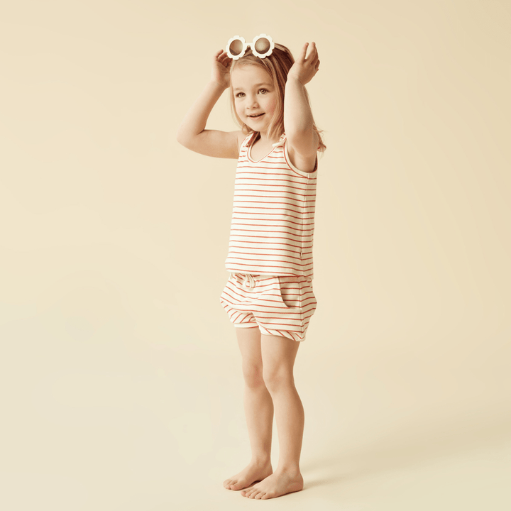 Wilson & Frenchy presents a little girl wearing a striped top and shorts, complemented by the Wilson & Frenchy Organic Rib Stripe Tie Kids Singlet (Multiple Variants). Complete the outfit with the Summer Stripe Woven Cot Blanket.