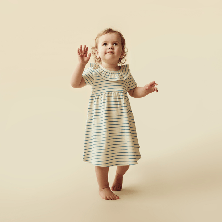 A baby girl in a blue and white striped Wilson & Frenchy Organic Stripe Rib Kids Ruffle Dress (Multiple Variants).