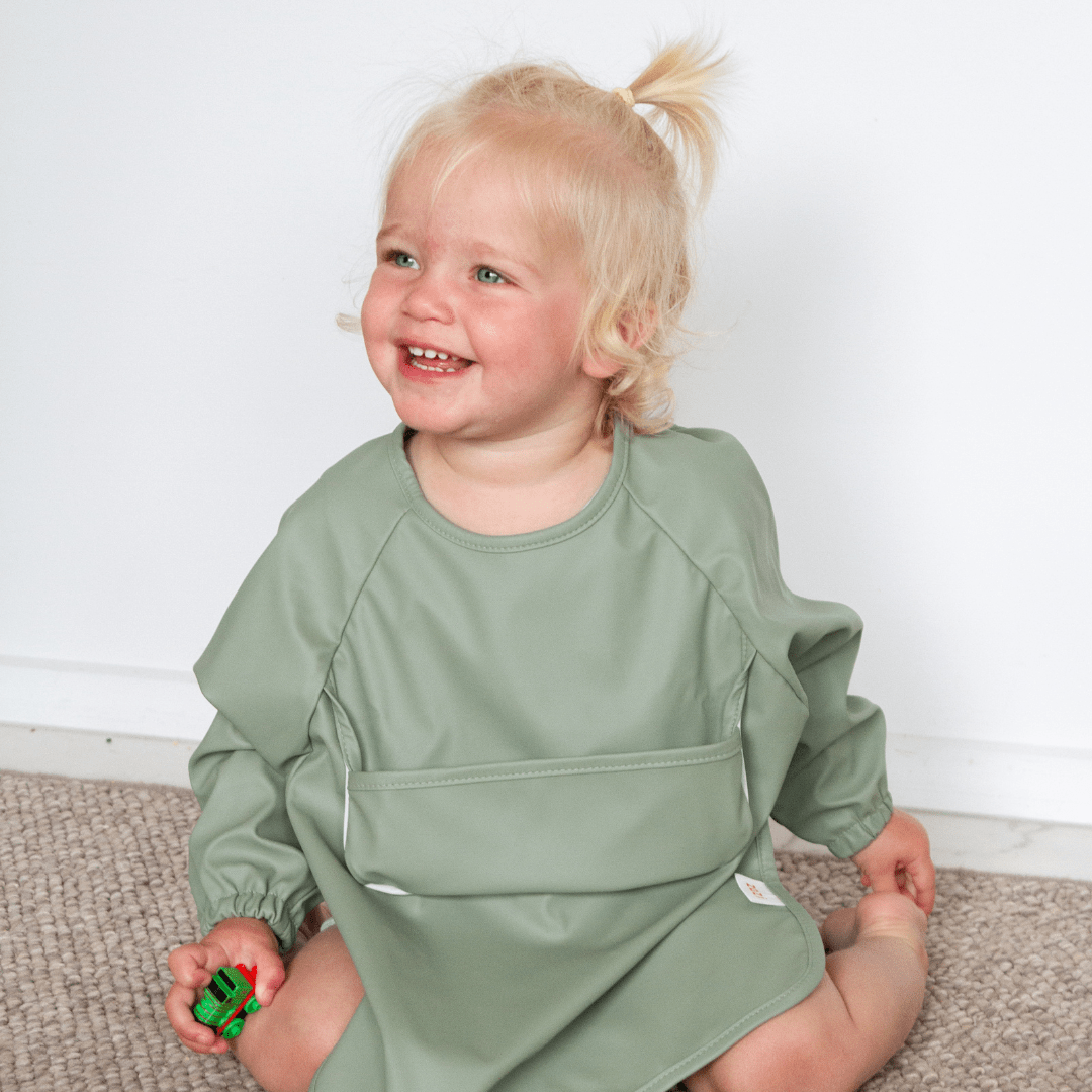 A little girl wearing a Zazi Recycled Full-Sleeved Bib (Multiple Variants) sitting on the floor.