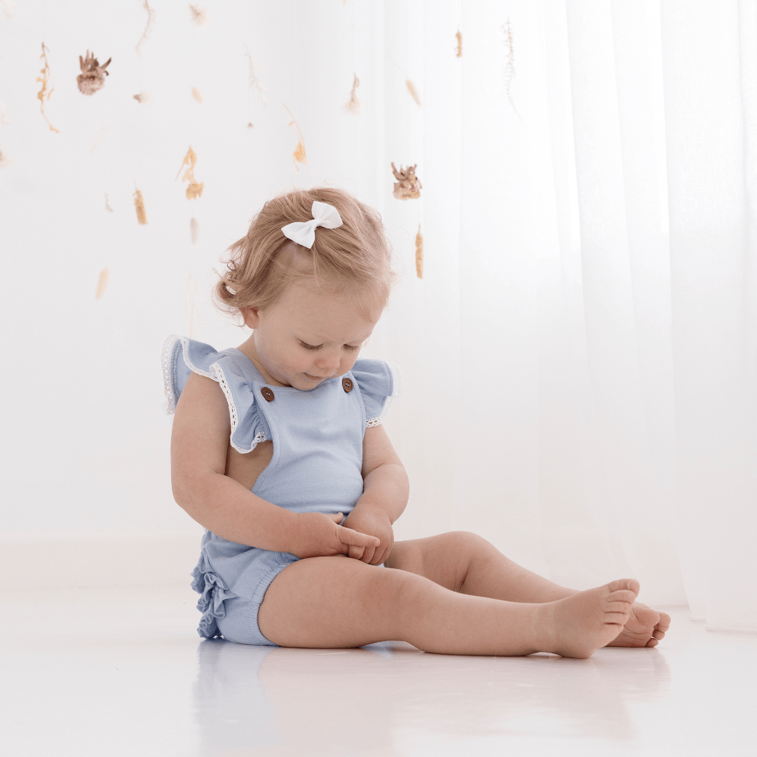 Little-Girl-With-Bow-Wearing-Aster-And-Oak-Organic-Cotton-Chambray-Ruffle-Playsuit-Naked-Baby-Eco-Boutique
