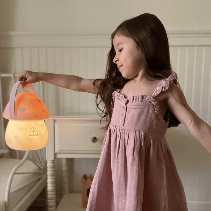 A little girl in a pink dress holding a Little Belle Nightlights Fairy House Carry Lantern.