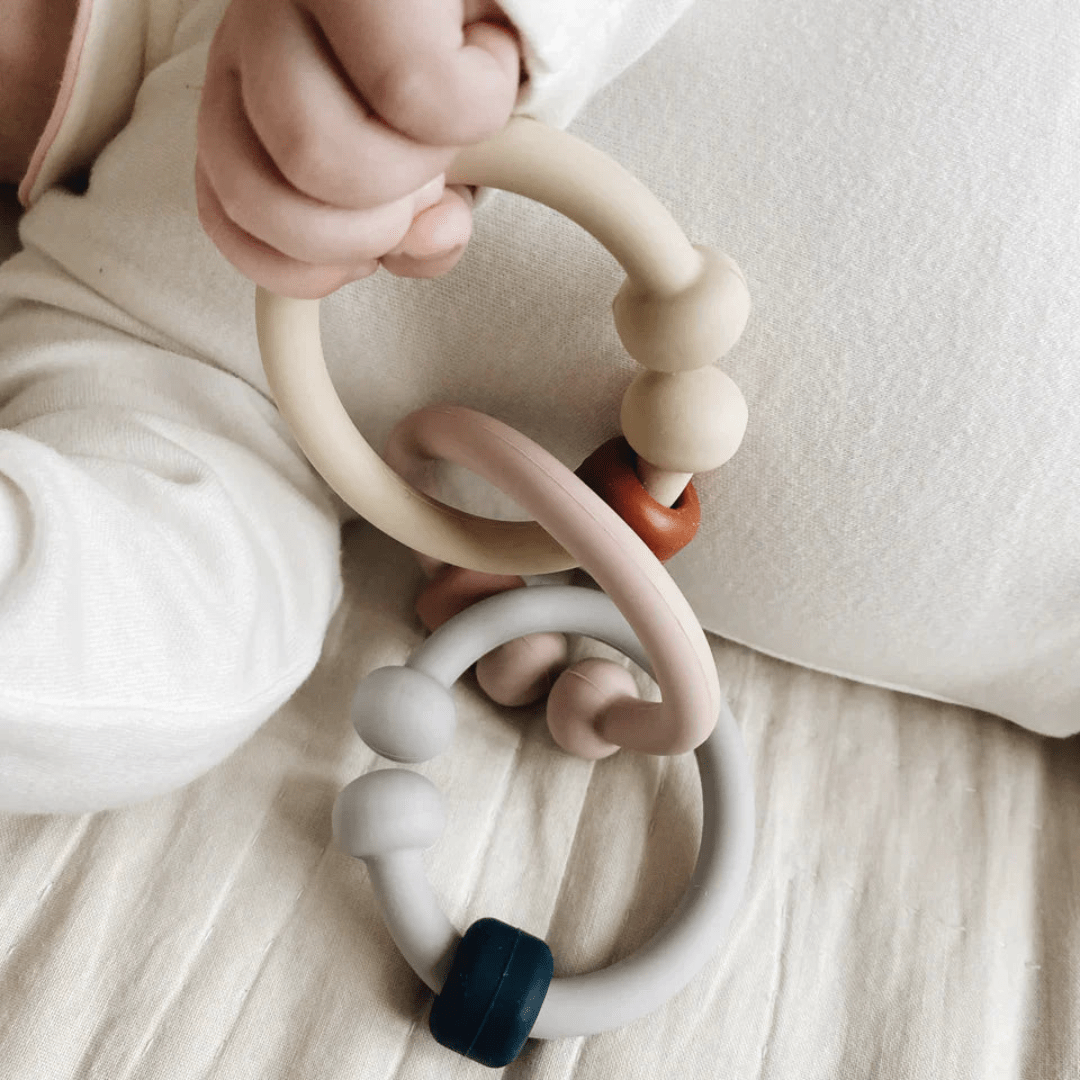 A baby is playing with a Classical Child silicone teether toy on a bed, finding teething relief.