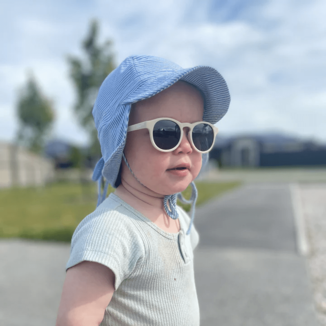 A baby wearing Zazi Shades Baby & Toddler Sunglasses by Zazi, with UV400 protection and polarized clarity, complemented by a hat.