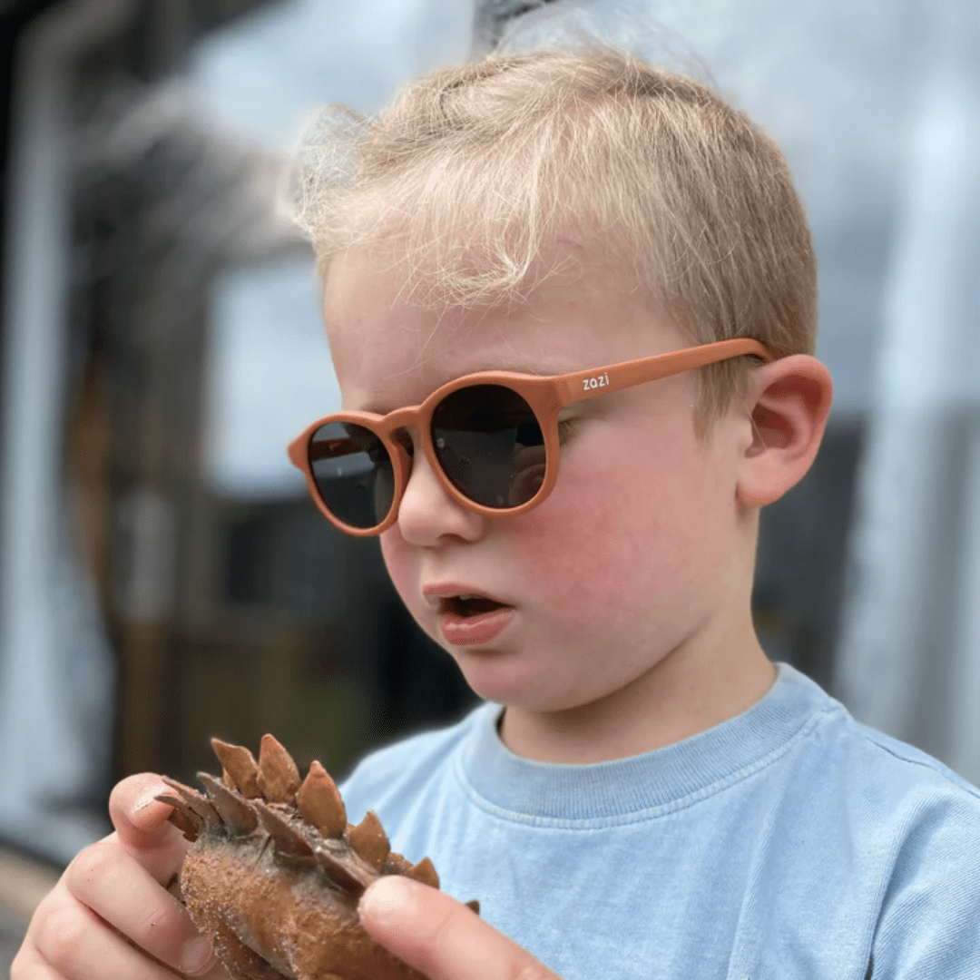 A young boy wearing Zazi Shades Baby & Toddler Sunglasses holding a shell.